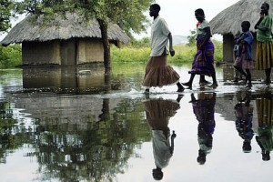 Ugandan women and children walk past submerged homes in an area flooded by heavy rains in Soroti, Uganda